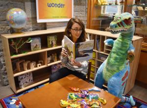 Lady reading in childrens play area to a toy dinosaur